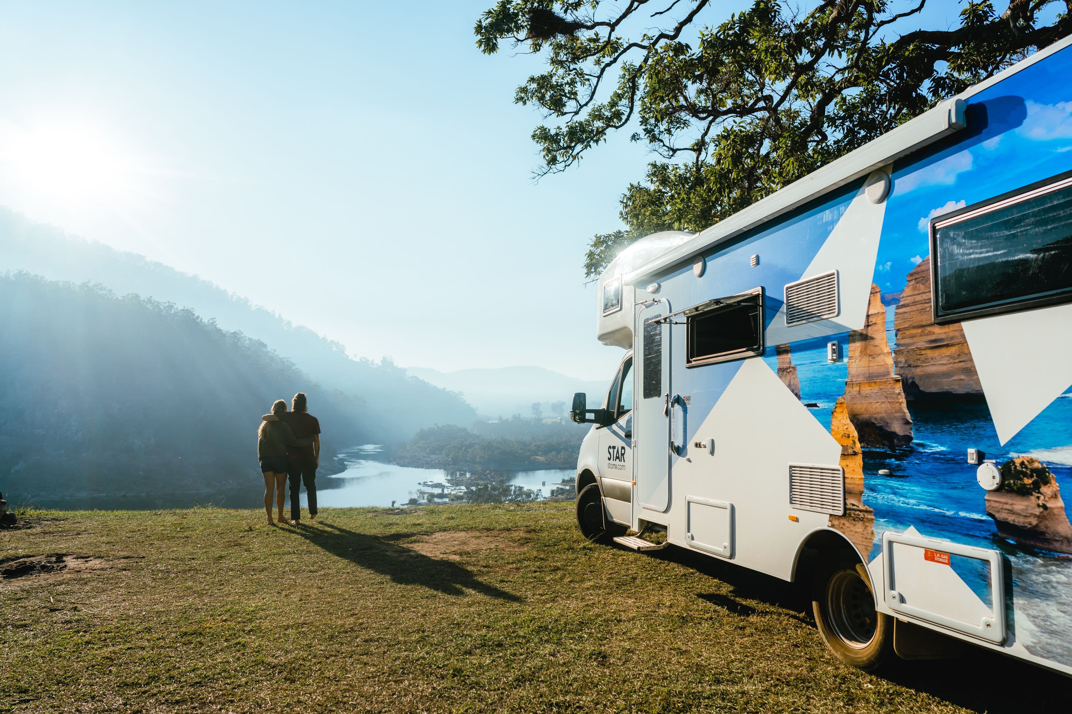 Two people standing by a motorhome looking over a cliff